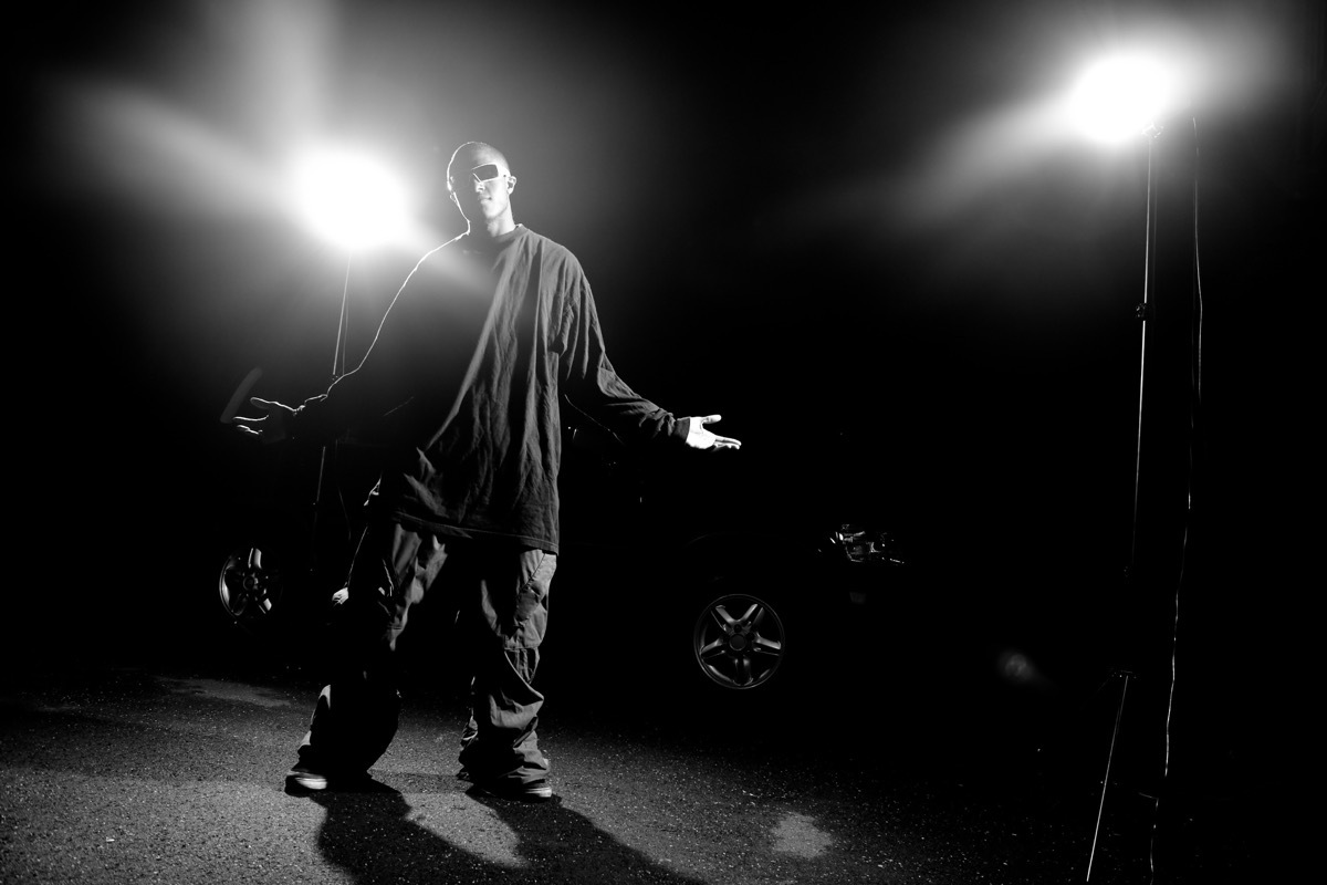 African American young man wearing baggy clothing posing under dramatic lighting with lens flare. - Image