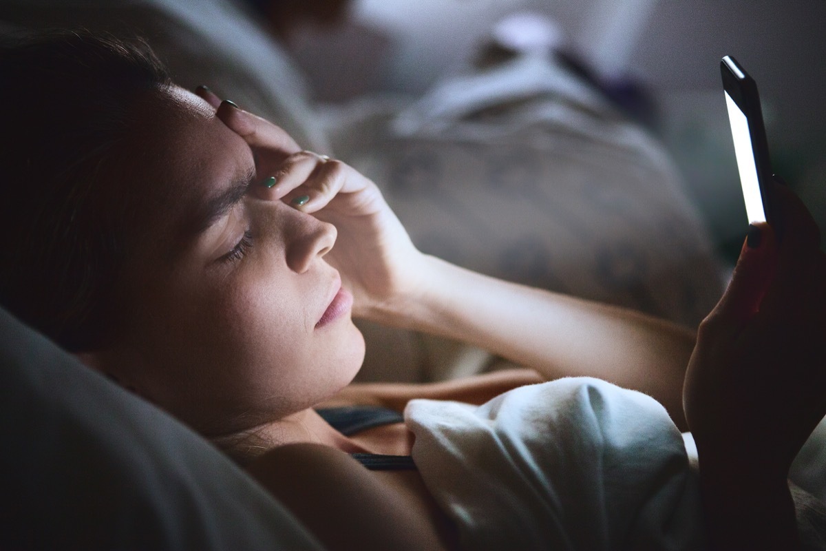 Woman lying in bed using her phone with head pain