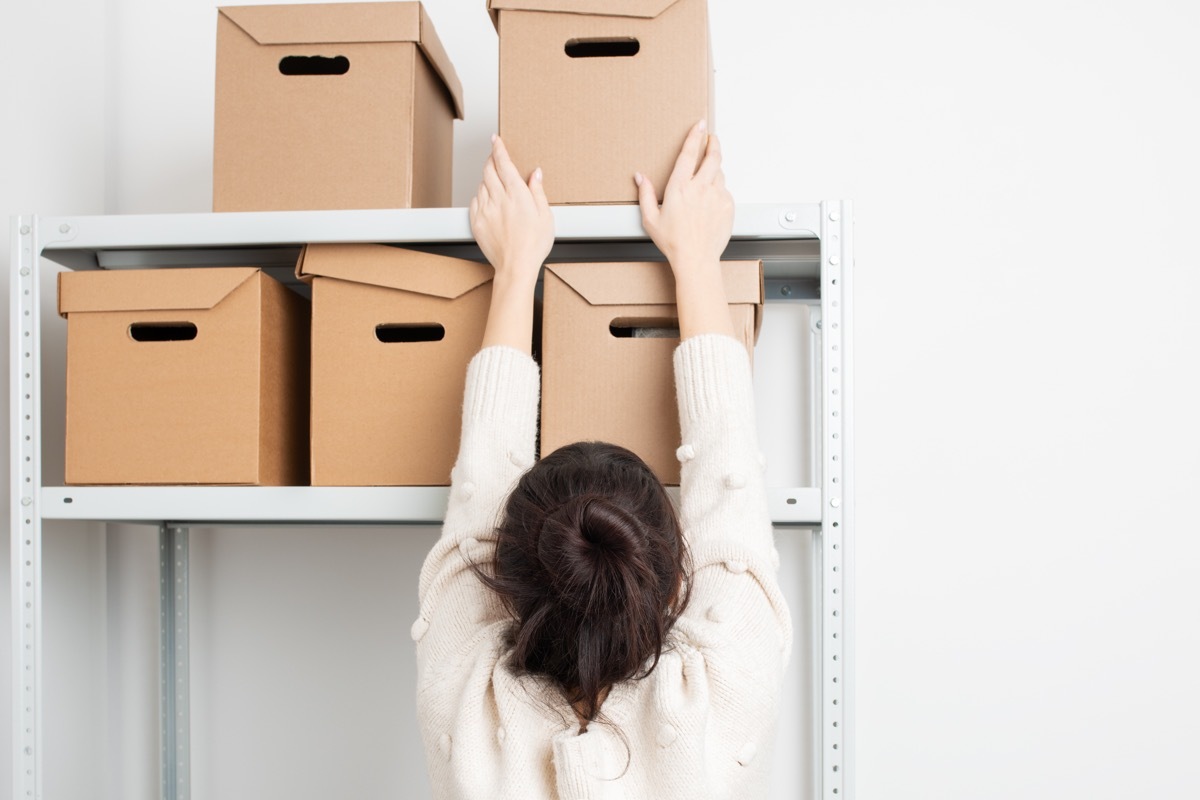 woman storing box on high shelf