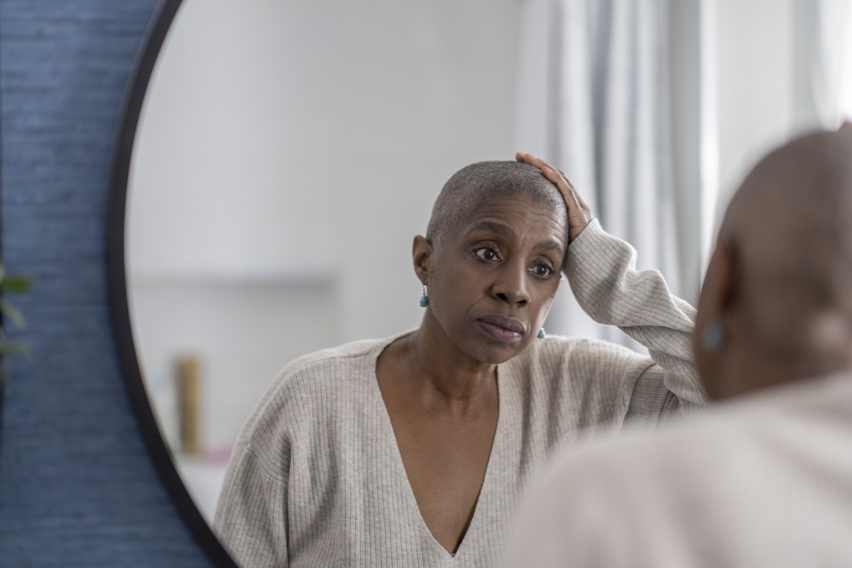 An elderly woman contemplates as she looks in the mirror and admires her new head shave.