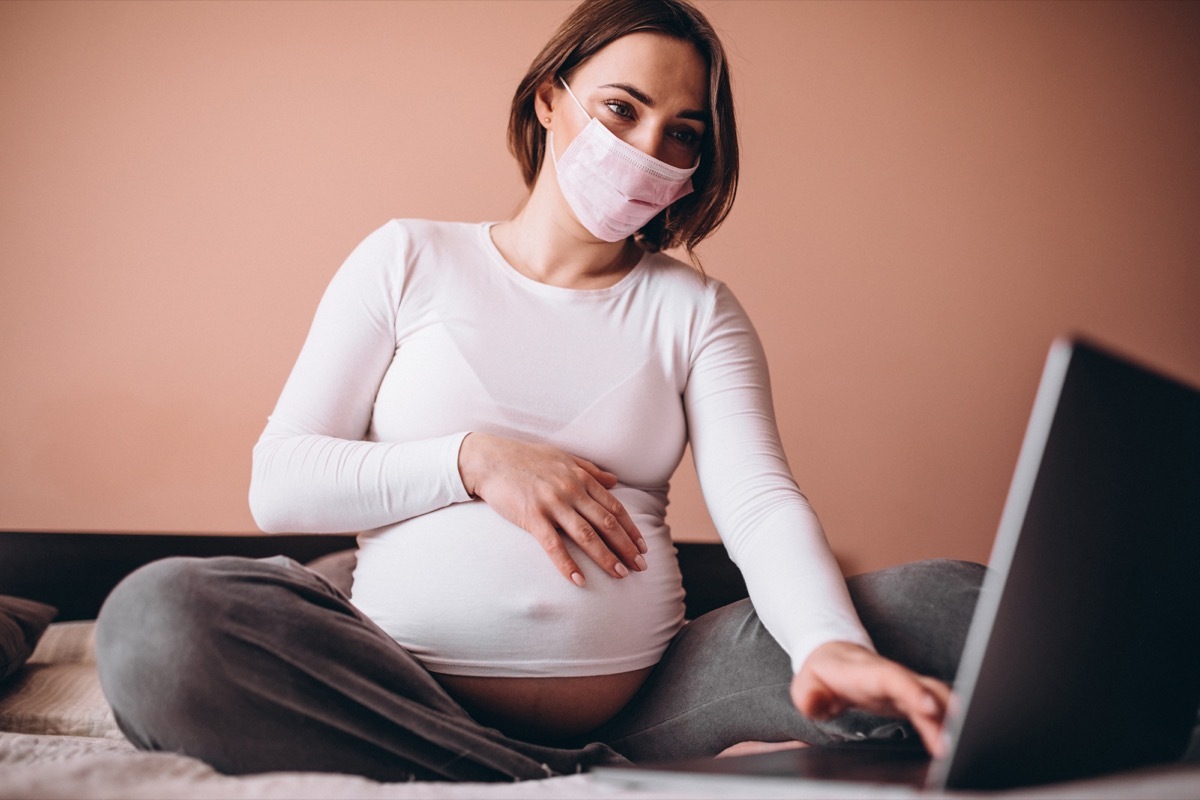 Pregnant woman with mask, using computer