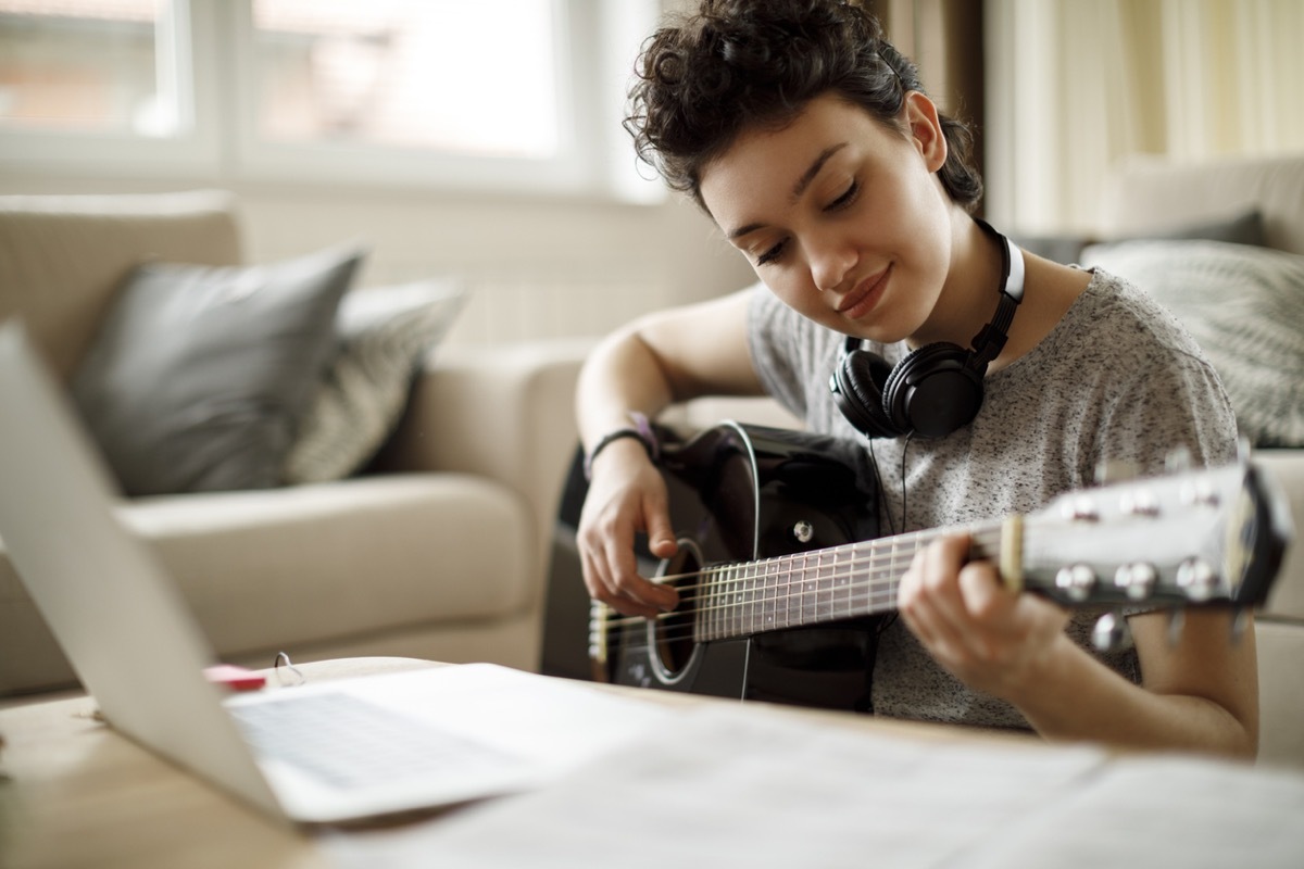 young girl playing guitar while looking at her computer