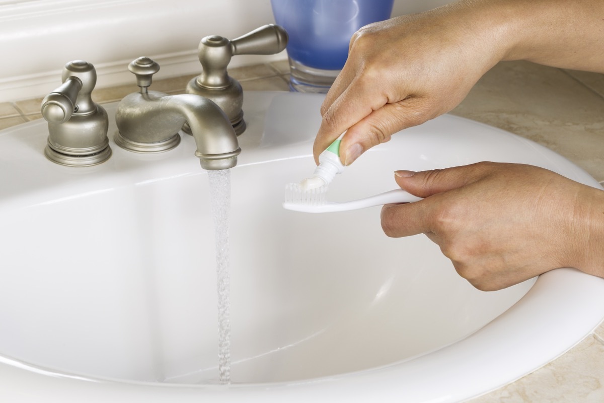 Sink running while putting toothpaste on toothbrush