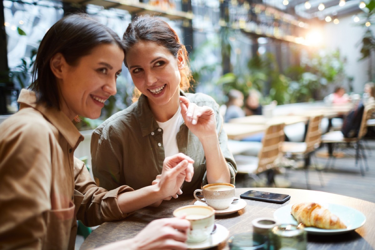 women whispering to each other at dining table