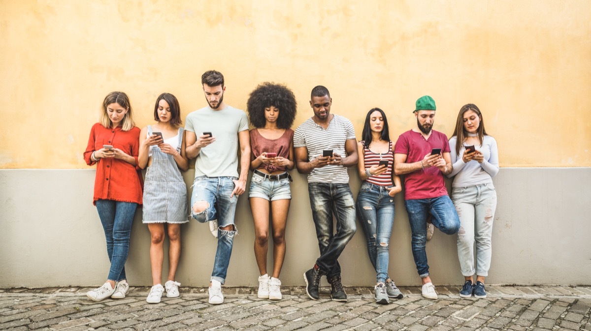 young friends against a wall using their phones