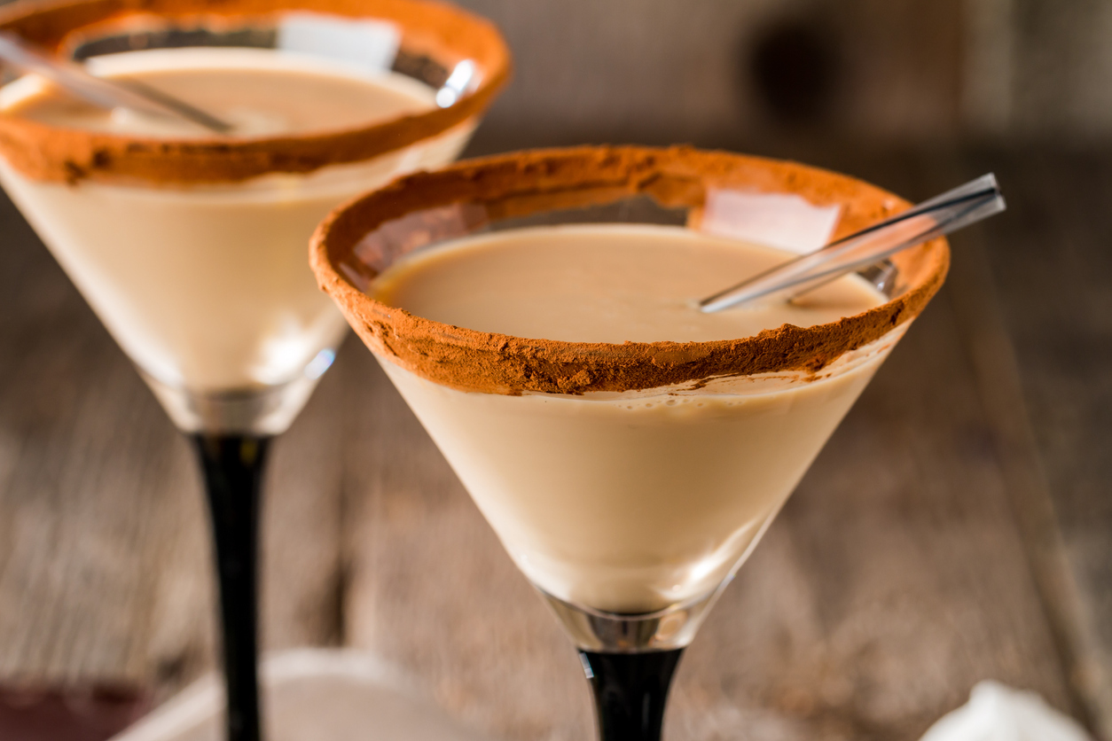 Irish cream liqueur in a glass with cinnamon on wooden background