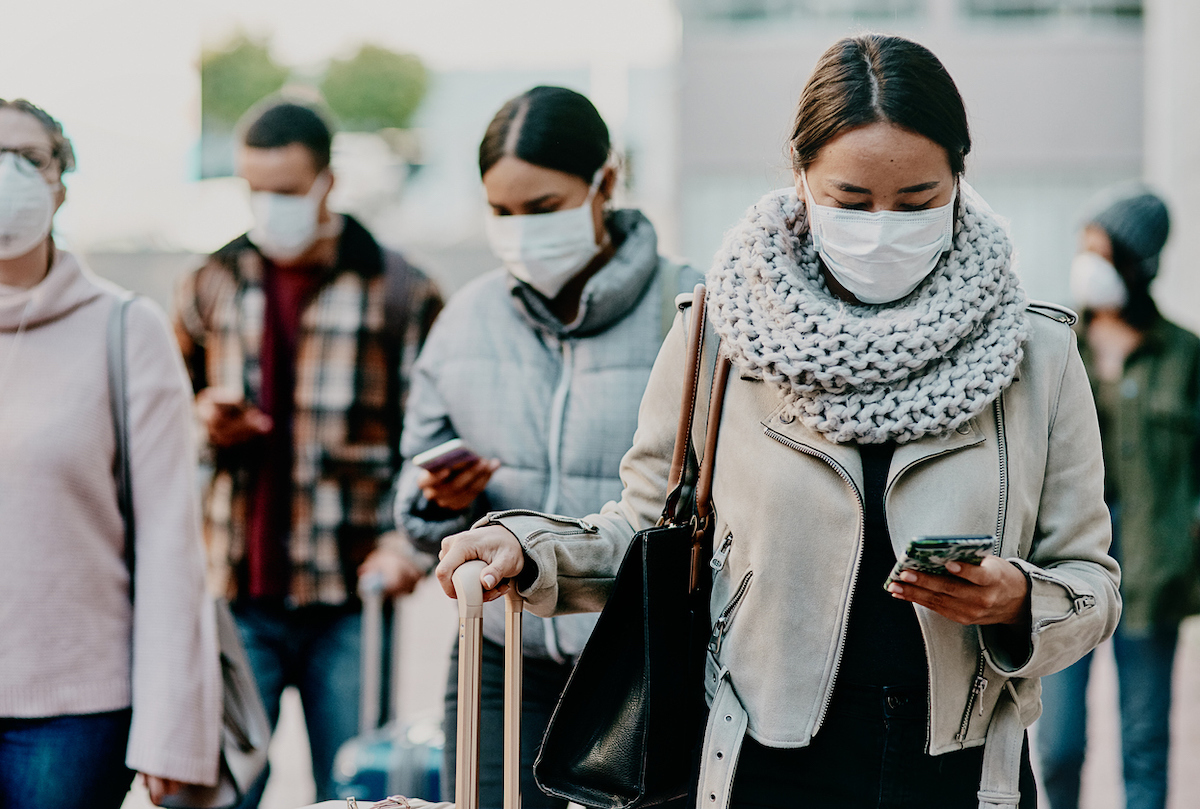 Shot of a young woman using a smartphone and wearing a mask while traveling