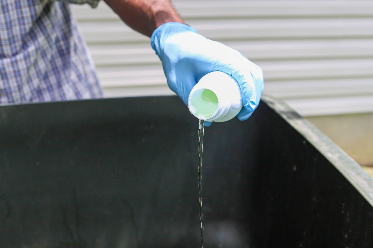 Hand pouring bleach into a sink.