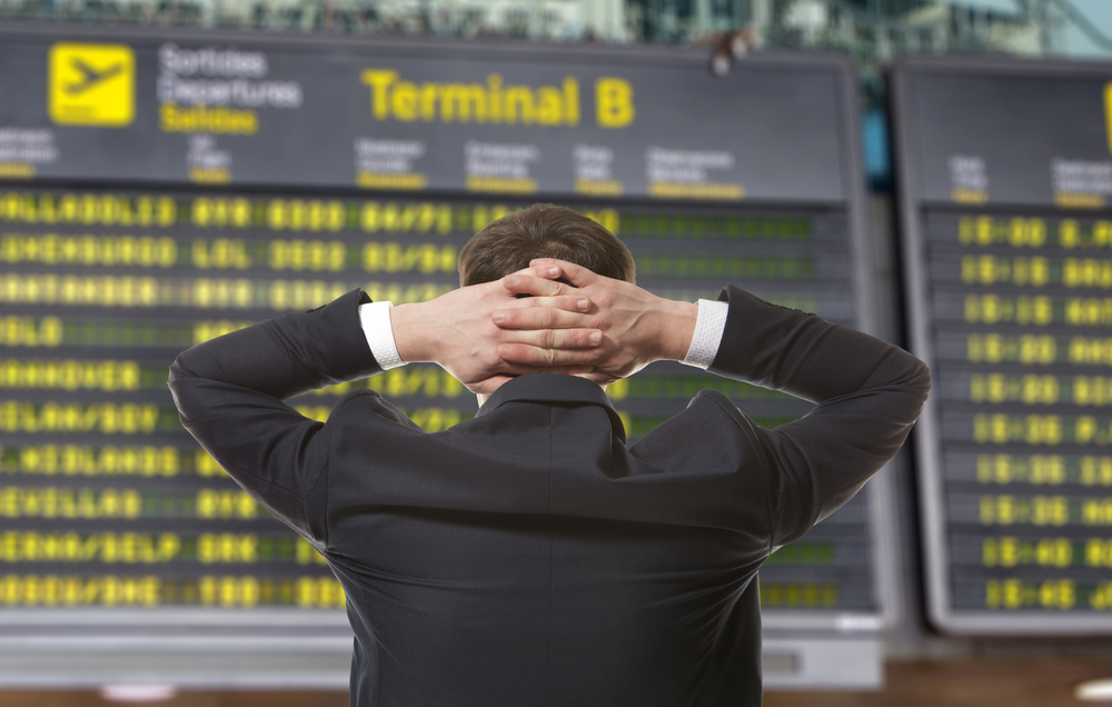 A man looking at an airline departure board with his hands behind his head