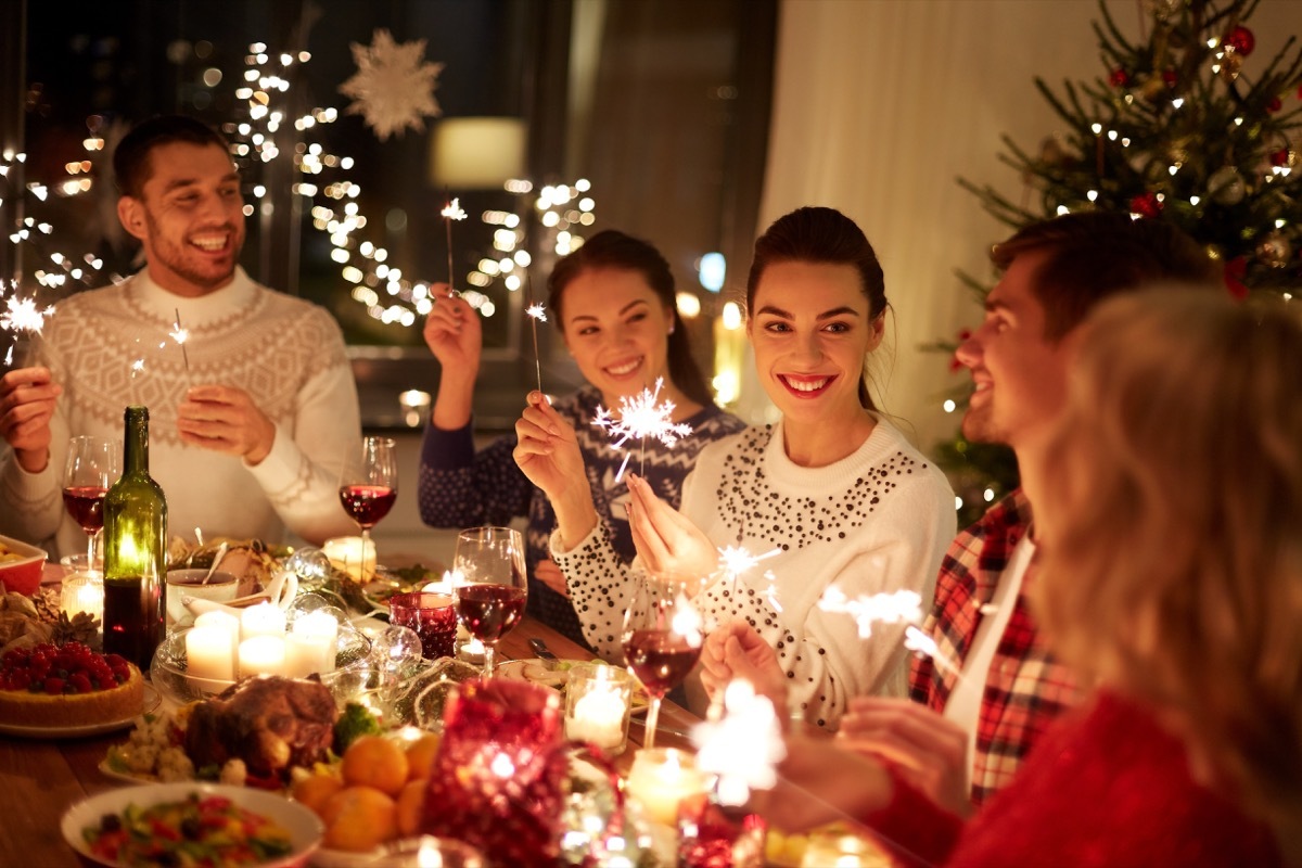 young people gathered around the christmas dinner table, holding sparklers