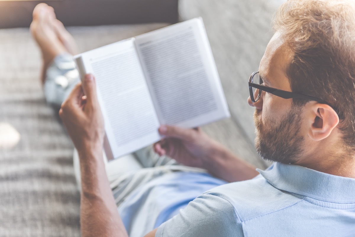 Man laying on a couch and reading a book