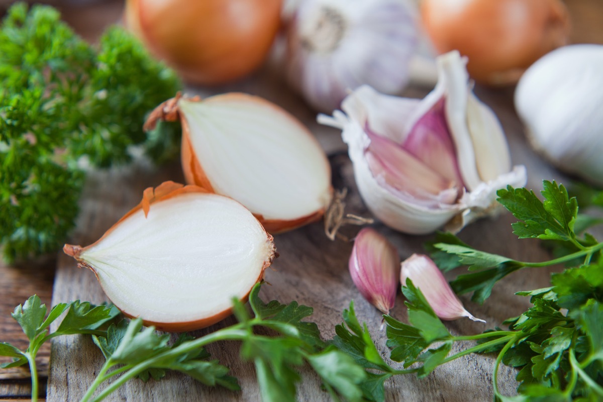 Garlic cloves, shallots and white onions - food ingredient on wooden board, decorated with fresh parsley.