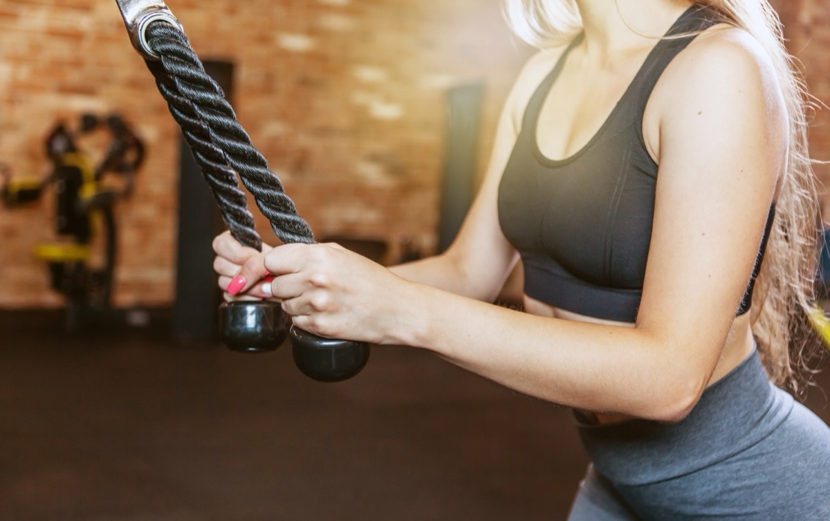 Woman training triceps. Young attractive woman with perfect body doing exercise with cable exercise machine in the gym