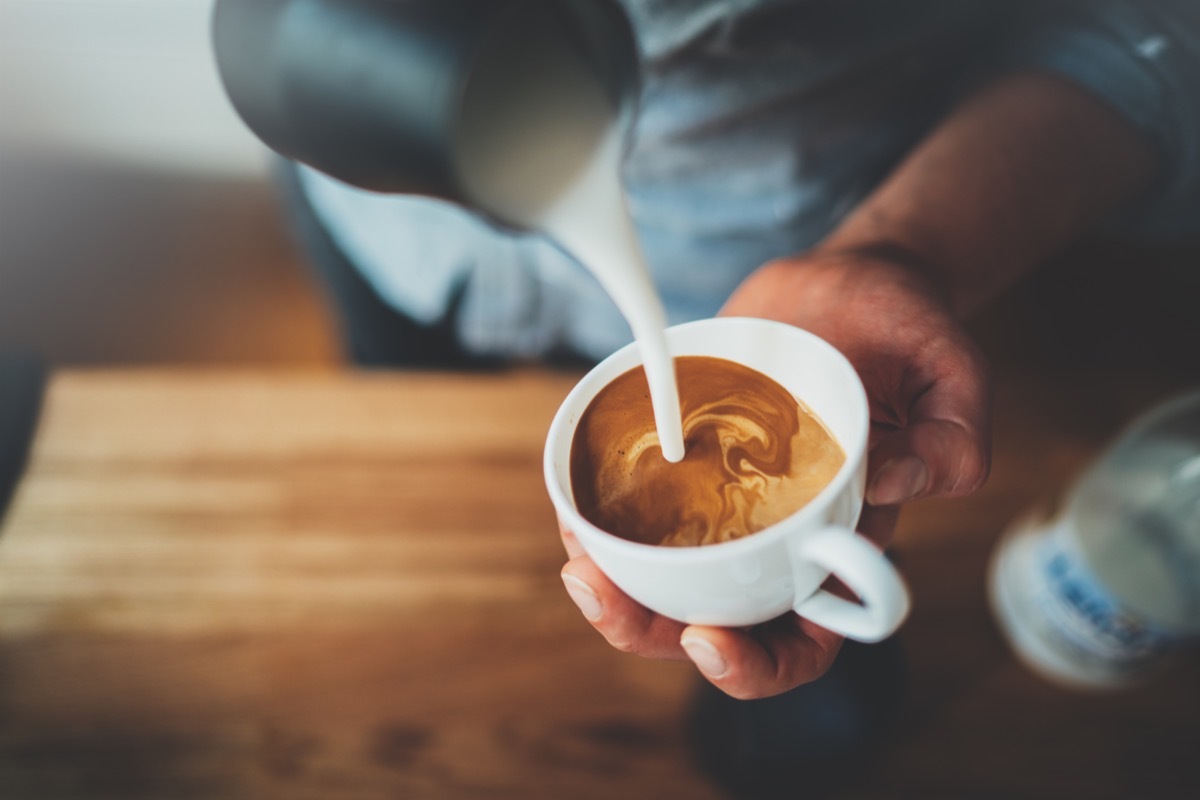 Close-up on hands of male barista pouring latte