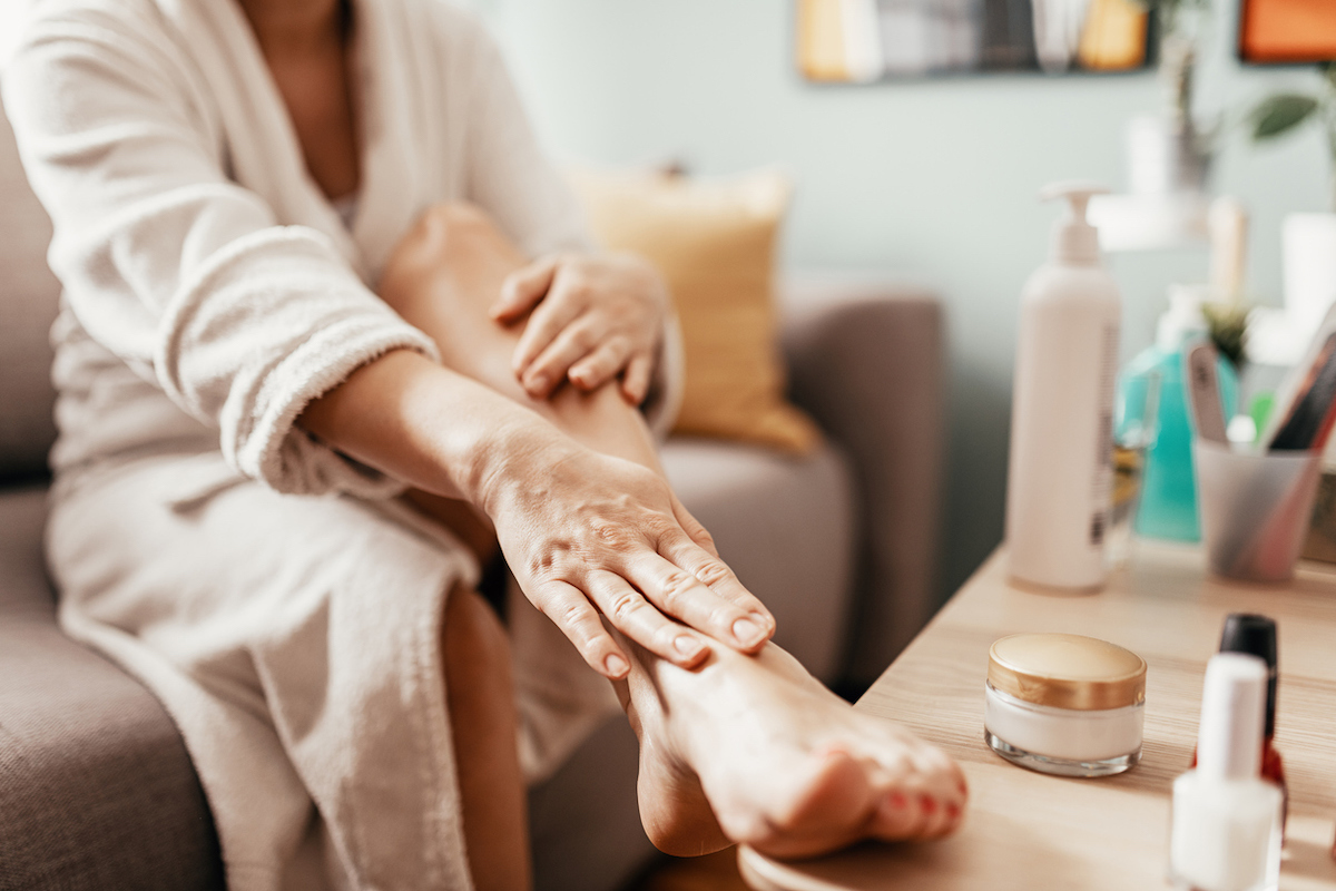 Close up of a woman applying lotion to her leg that's propped on a table.