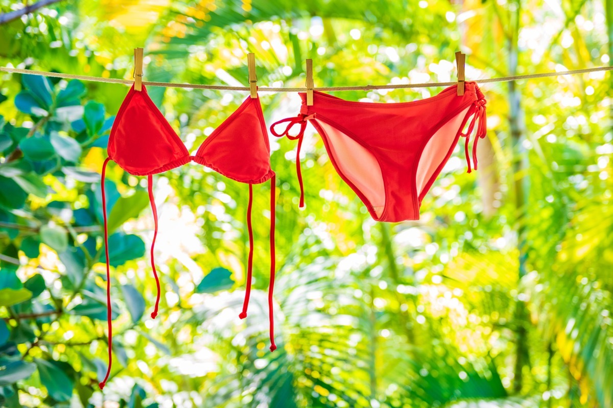 Red bikini swimsuit hanging air drying on clothing line outside on balcony. Summer vacation icon background - woman swimwear eco friendly laundry outdoor with green plants.