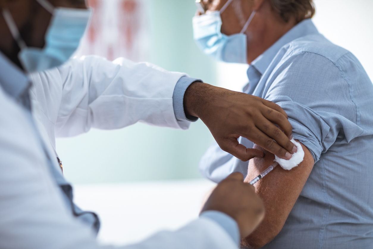 A man wearing a face mask gets a COVID-19 vaccine injected into his arm by a male doctor.