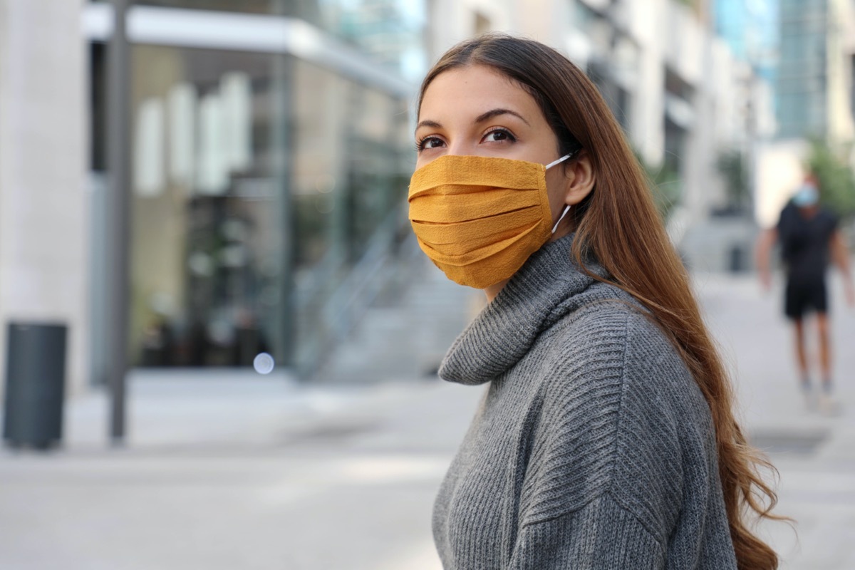 Woman with protective mask looks around on a street.