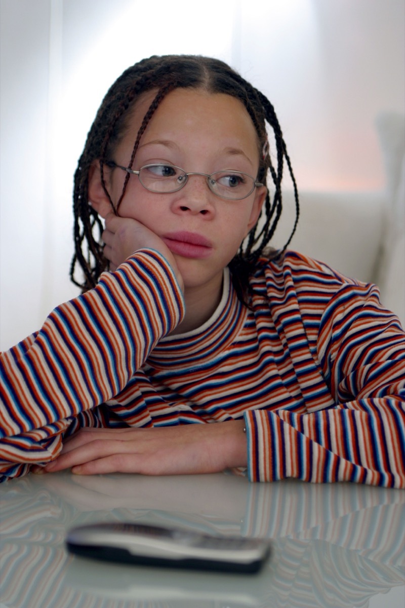 Unhappy child sit at table contemplating and 1990s cell phone on the table.