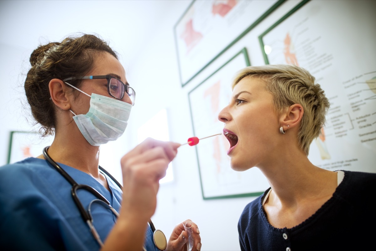 Side close view of female doctor specialist with face mask holding buccal cotton swab and test tube ready to collect DNA from the cells on the inside of a woman patient