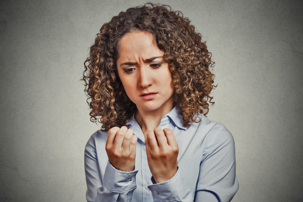 young woman with curly hair looks at her fingernails with a concerned expression on her face