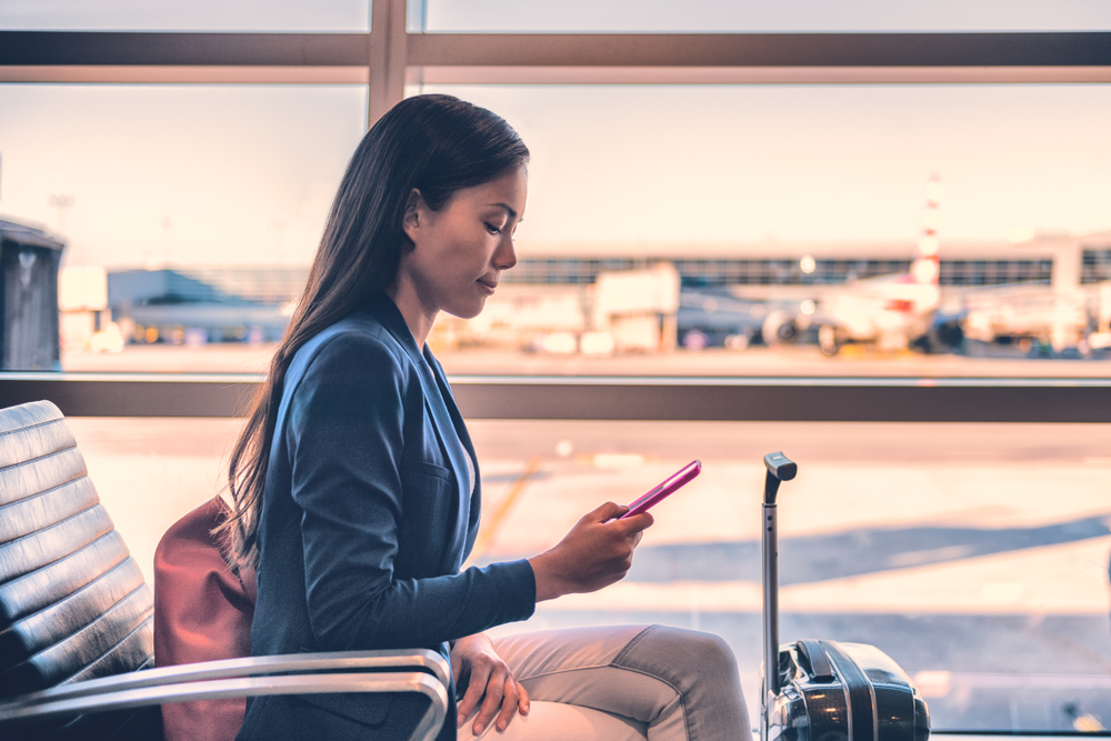 A woman using her phone while seated in an airport terminal waiting to board a flight