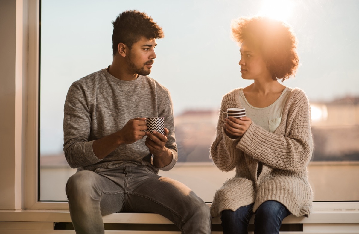 couple having a conversation during coffee time while relaxing on a window sill.