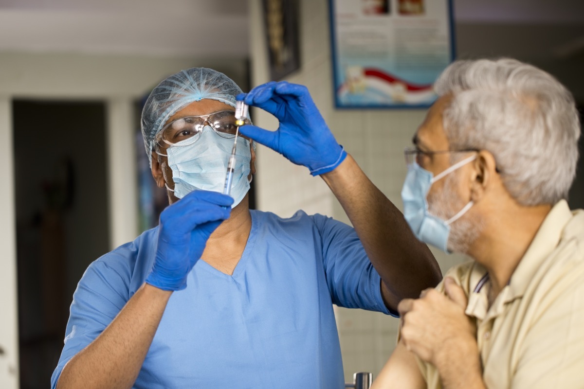 Doctor in surgical gloves pulling vaccine liquid from vial to vaccinate male patient