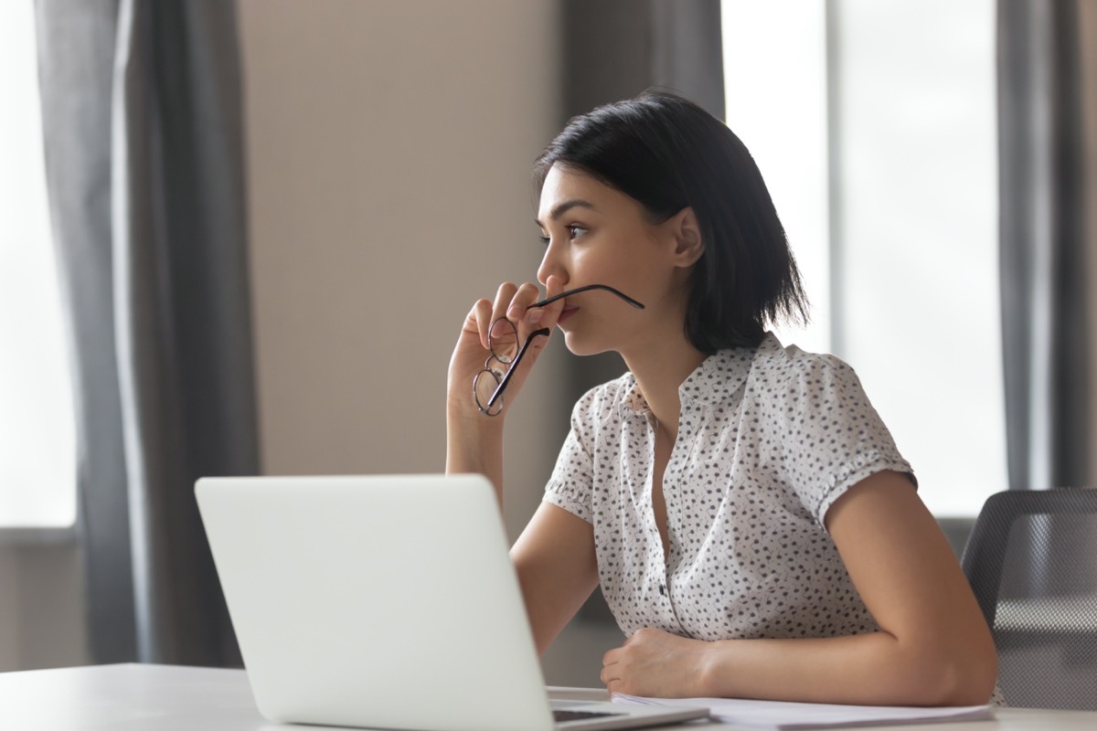 Thoughtful anxious business woman looking away thinking solving problem at work, worried serious young chinese woman concerned make difficult decision lost in thought reflecting sit with laptop