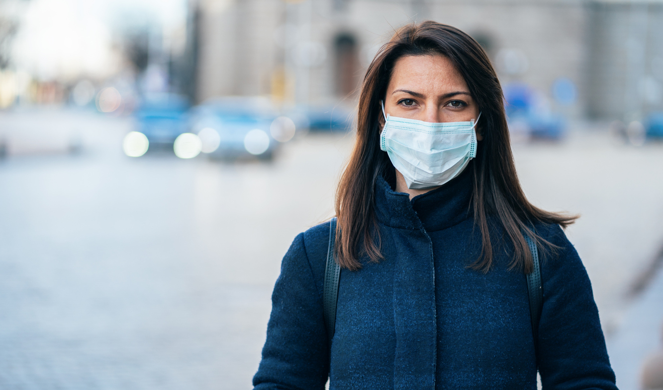 A woman wearing a warm jacket and a face mask while standing outside in a city.