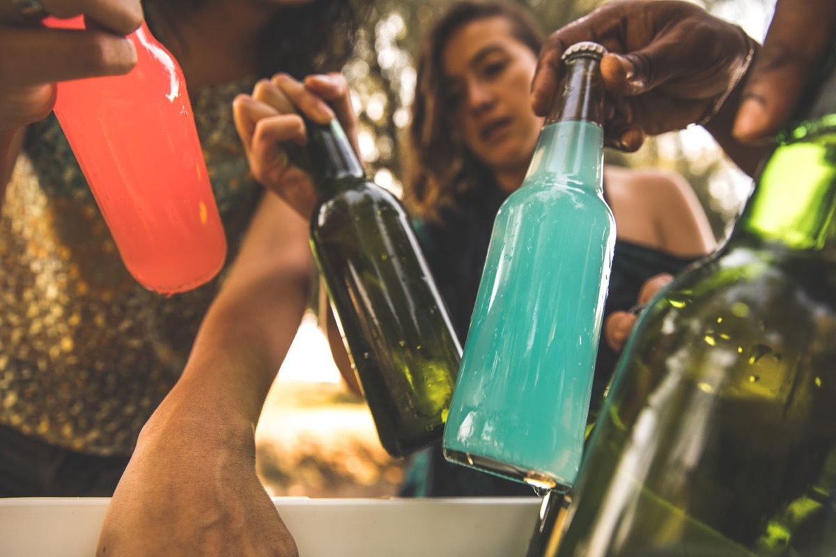 Close up shot of group of young people taking out bottles of beverages from a cooler, to enjoy during their picnic.