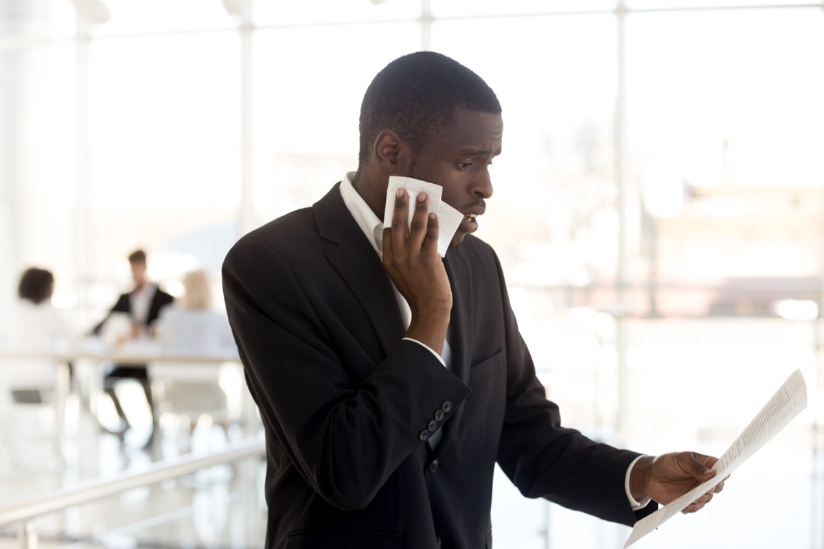 Nervous black man wipes off sweat at office, signs you stress people out