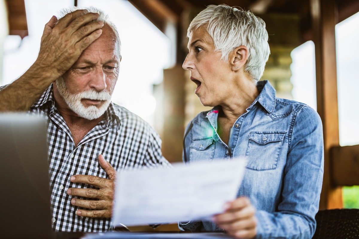 Shocked senior couple reading their home finances in disbelief at balcony.