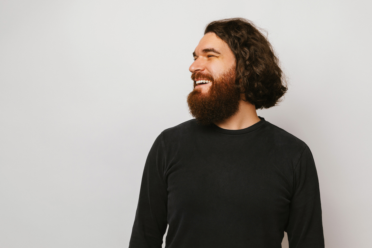 Man with long hair and a beard wearing a black shirt against a light gray background