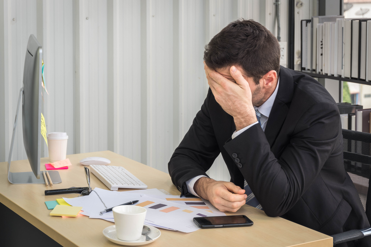 Bearded white man who is tired at his desk at work, with his face in his hand