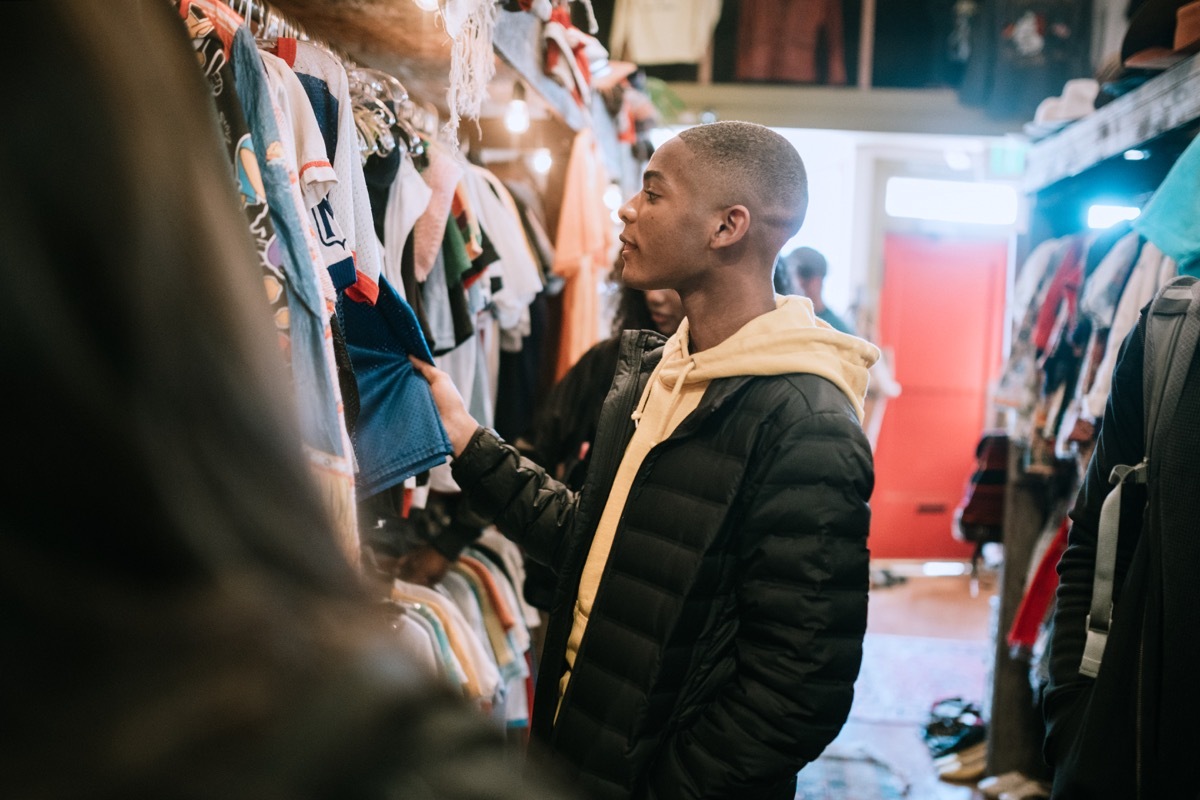 A smiling group of young adults have fun shopping for retro and vintage clothing styles at a second hand thrift store. Mixed ethnic group. Horizontal image with copy space.