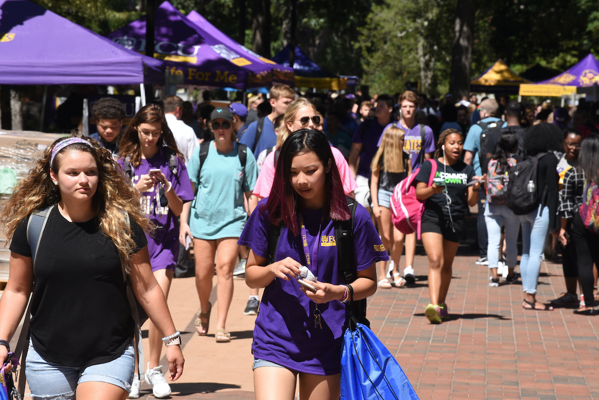 group of students walking outdoors on campus quad in purple clothing