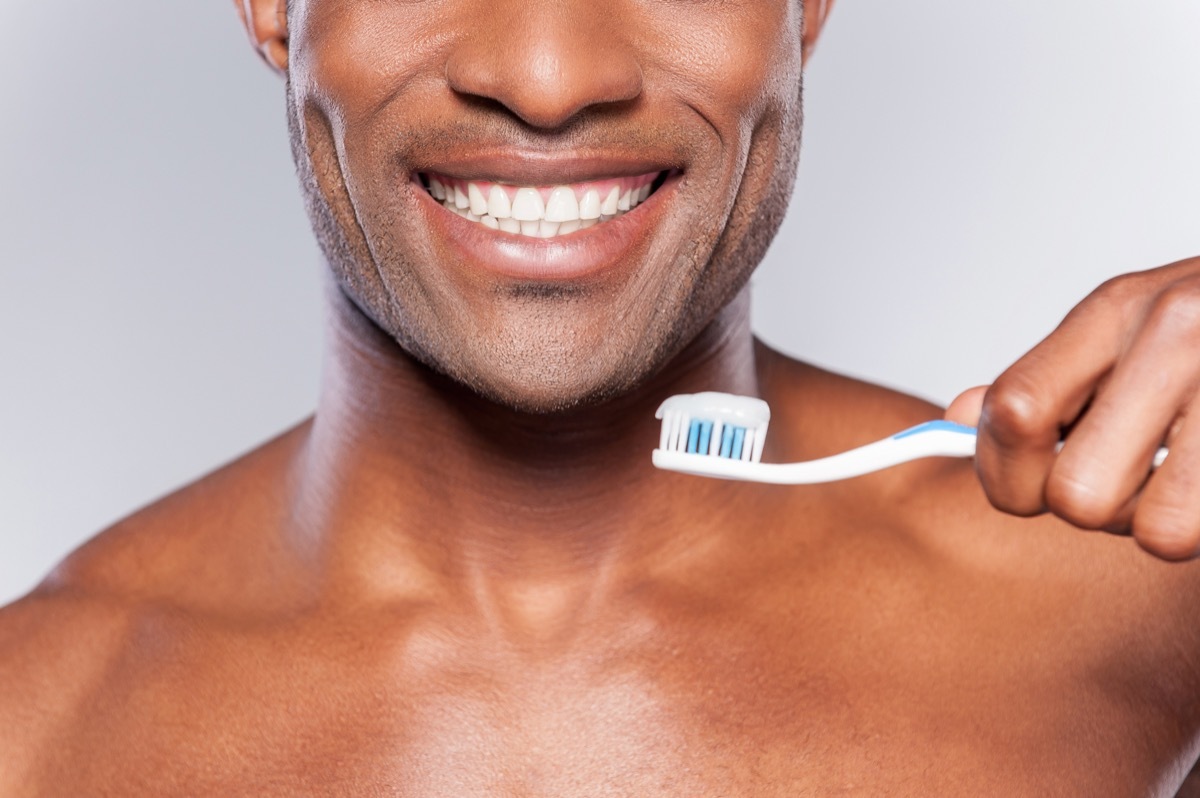 Man holding a toothbrush with toothpaste on it while smiling