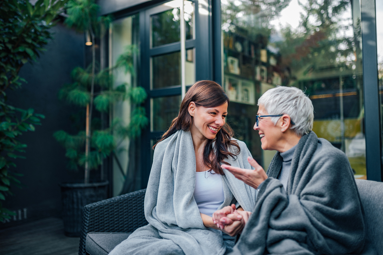 An older woman and younger woman sit on a patio talking to each other