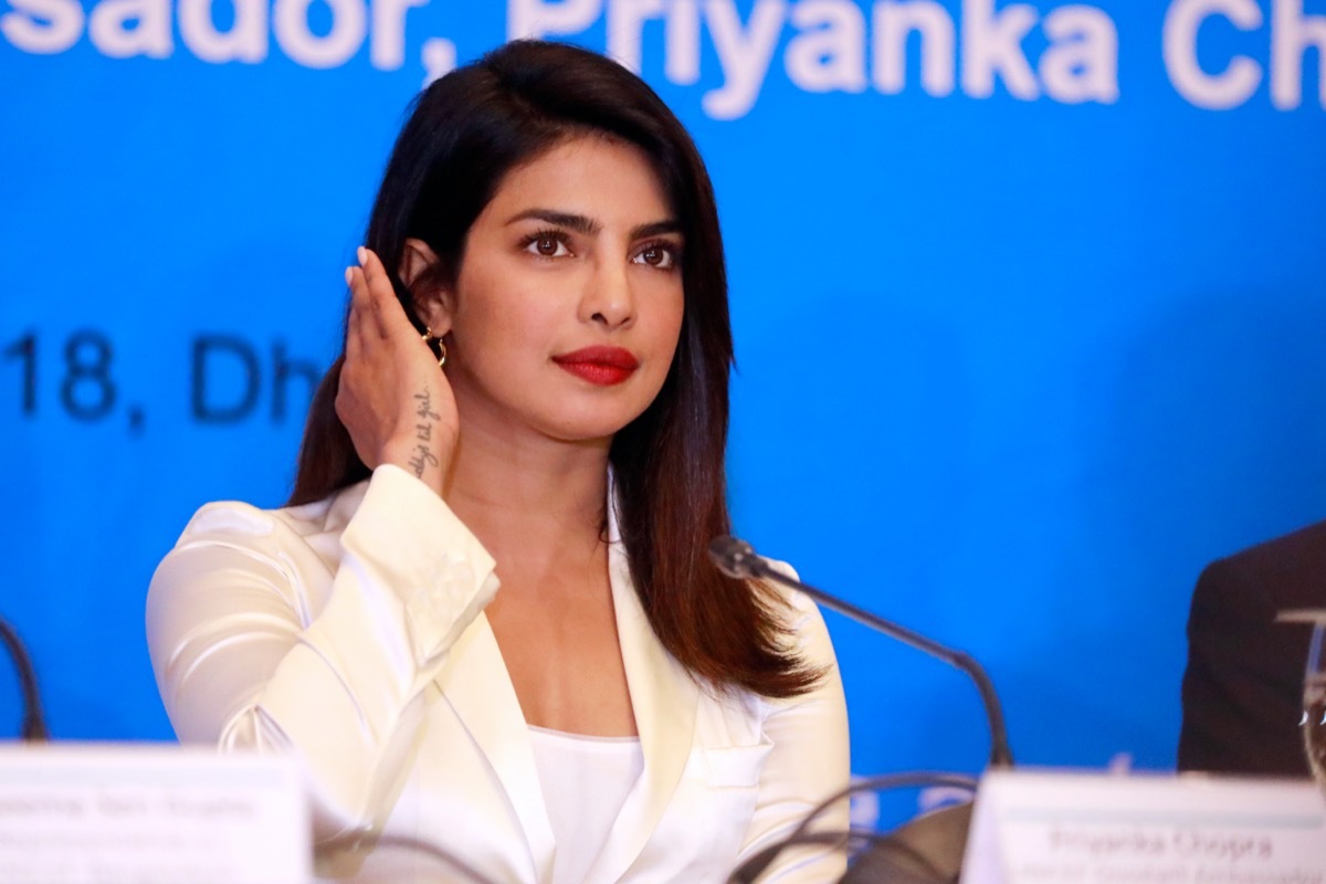 priyanka chopra in a white suit sitting at a desk