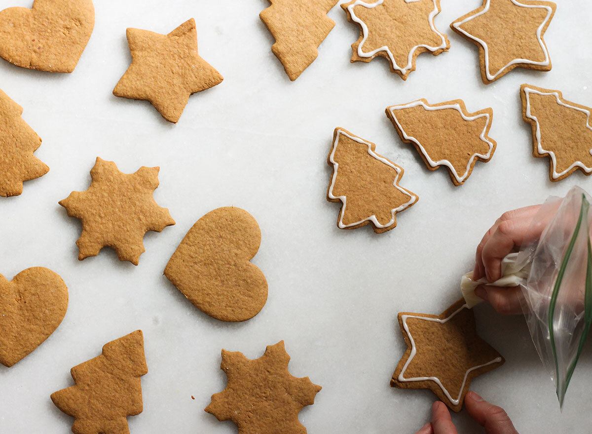 icing the edges of gingerbread cookies on a marble counter