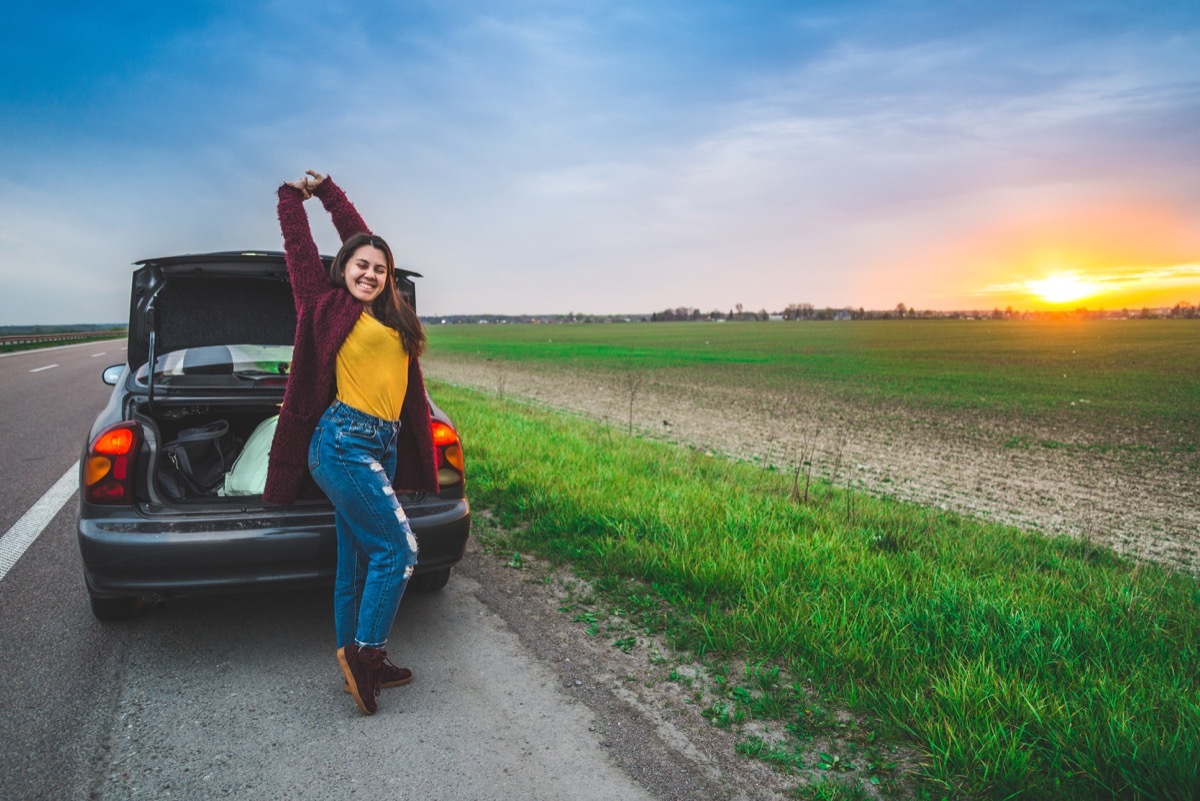 woman stratching near car on sunrise long car trip