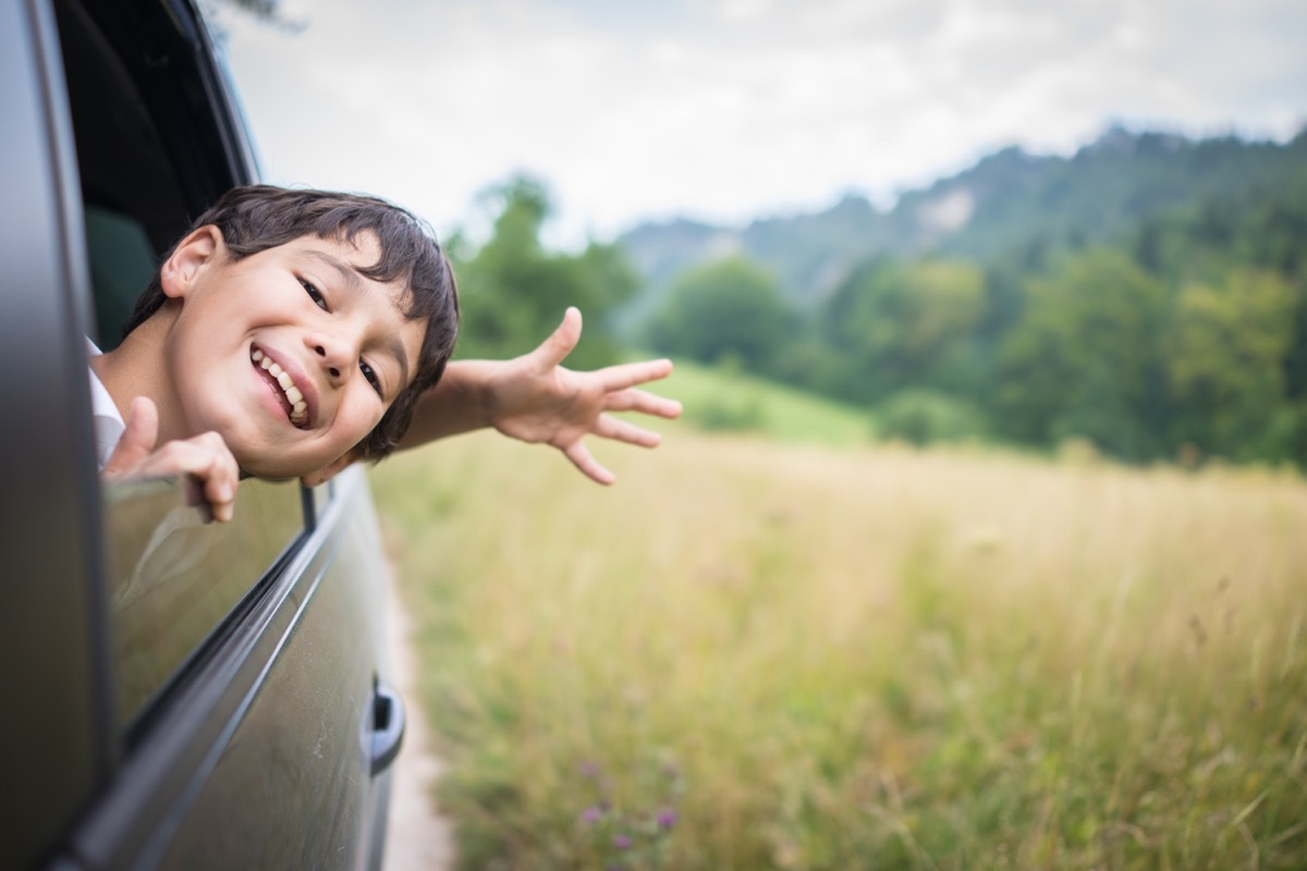 young boy with hand out the window of a car