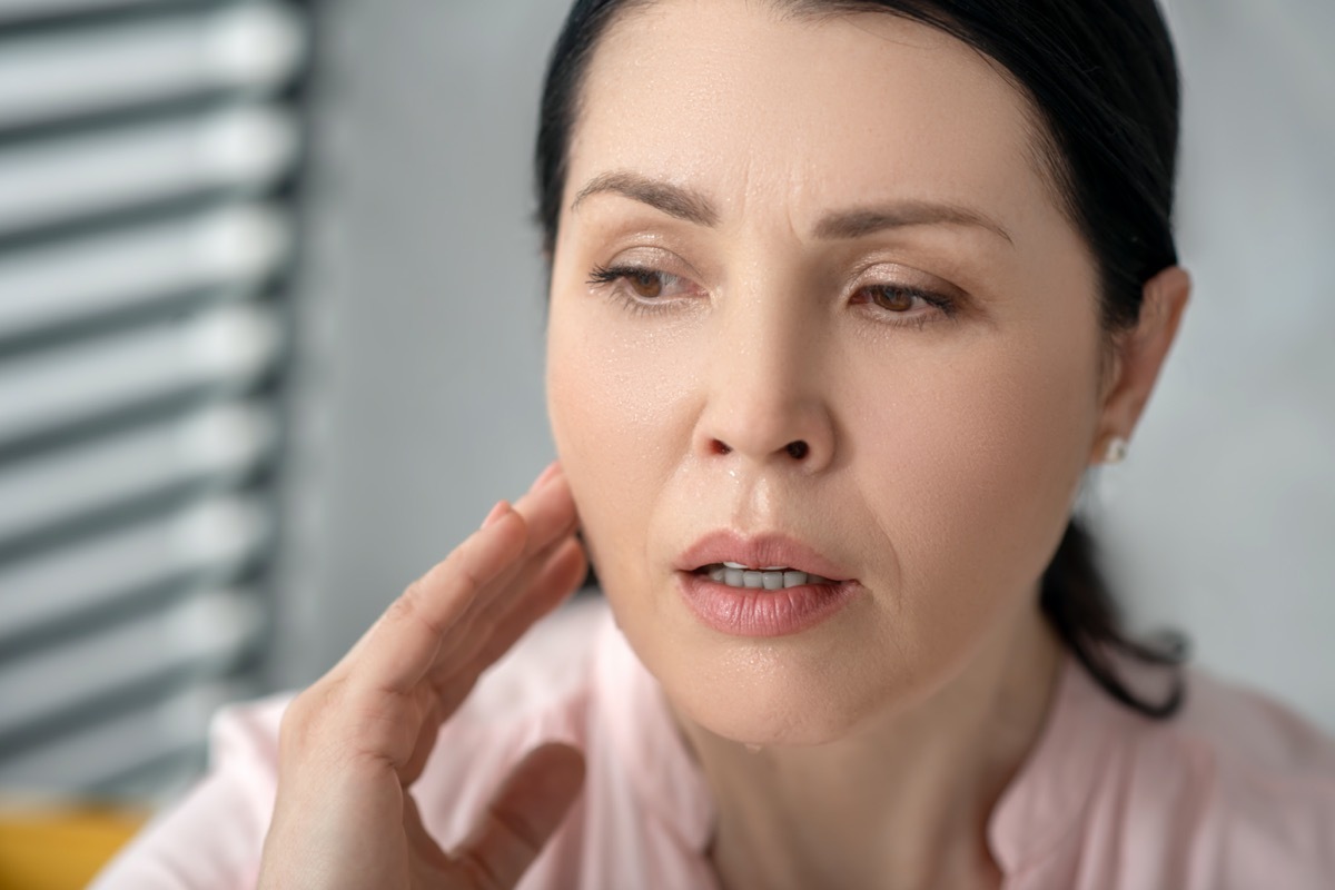 Face of a beautiful adult sad woman with long dark hair holding her hand near her neck.