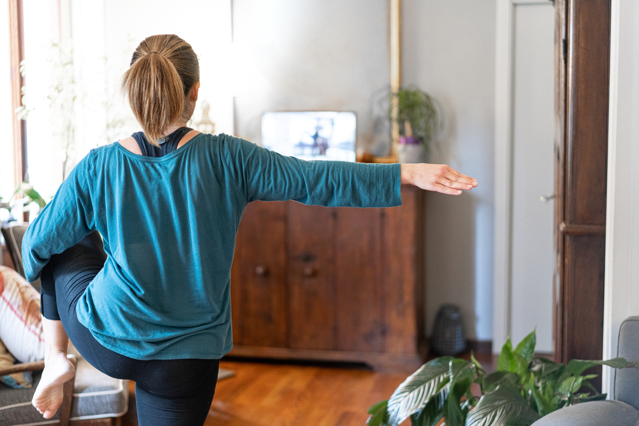 A young woman works out in her living room to a class on her laptop