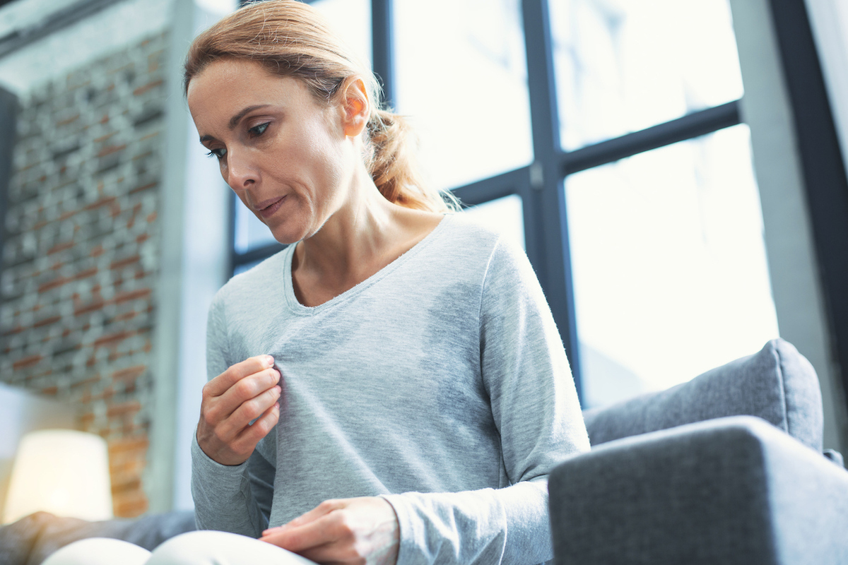 Middle aged woman touching sweater and sweating, possibly having a hot flash