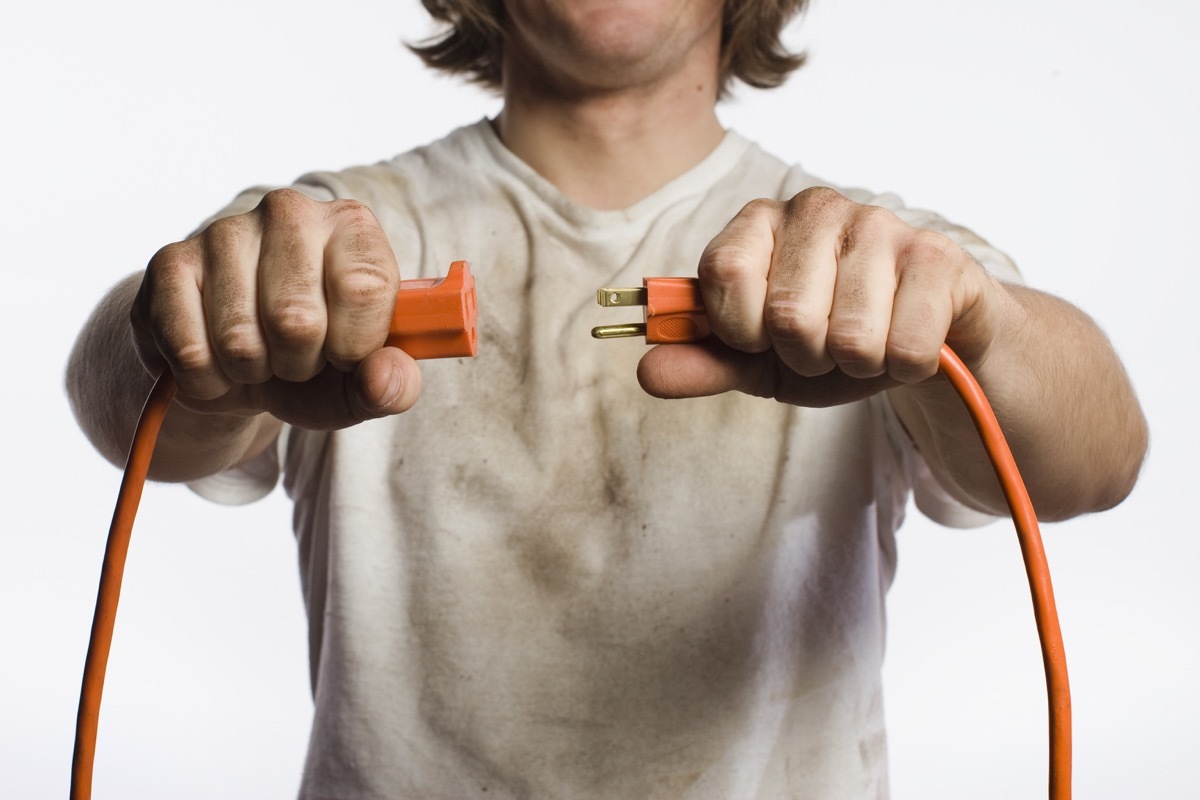 white guy in dirty clothes holding two ends of an extension cord