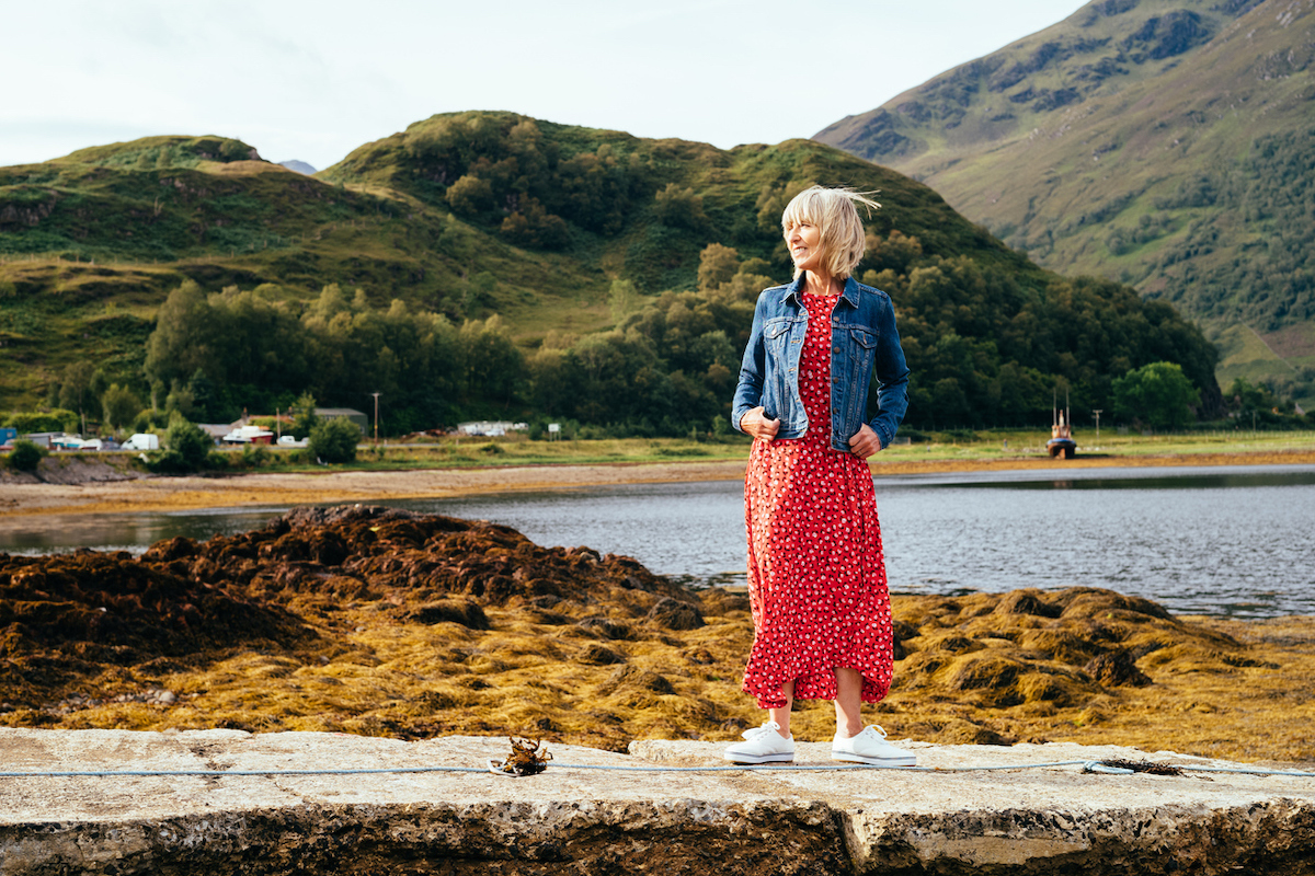 Woman wearing a red dress and denim jacket strolling on the jetty at Loch Duich, Scotland.