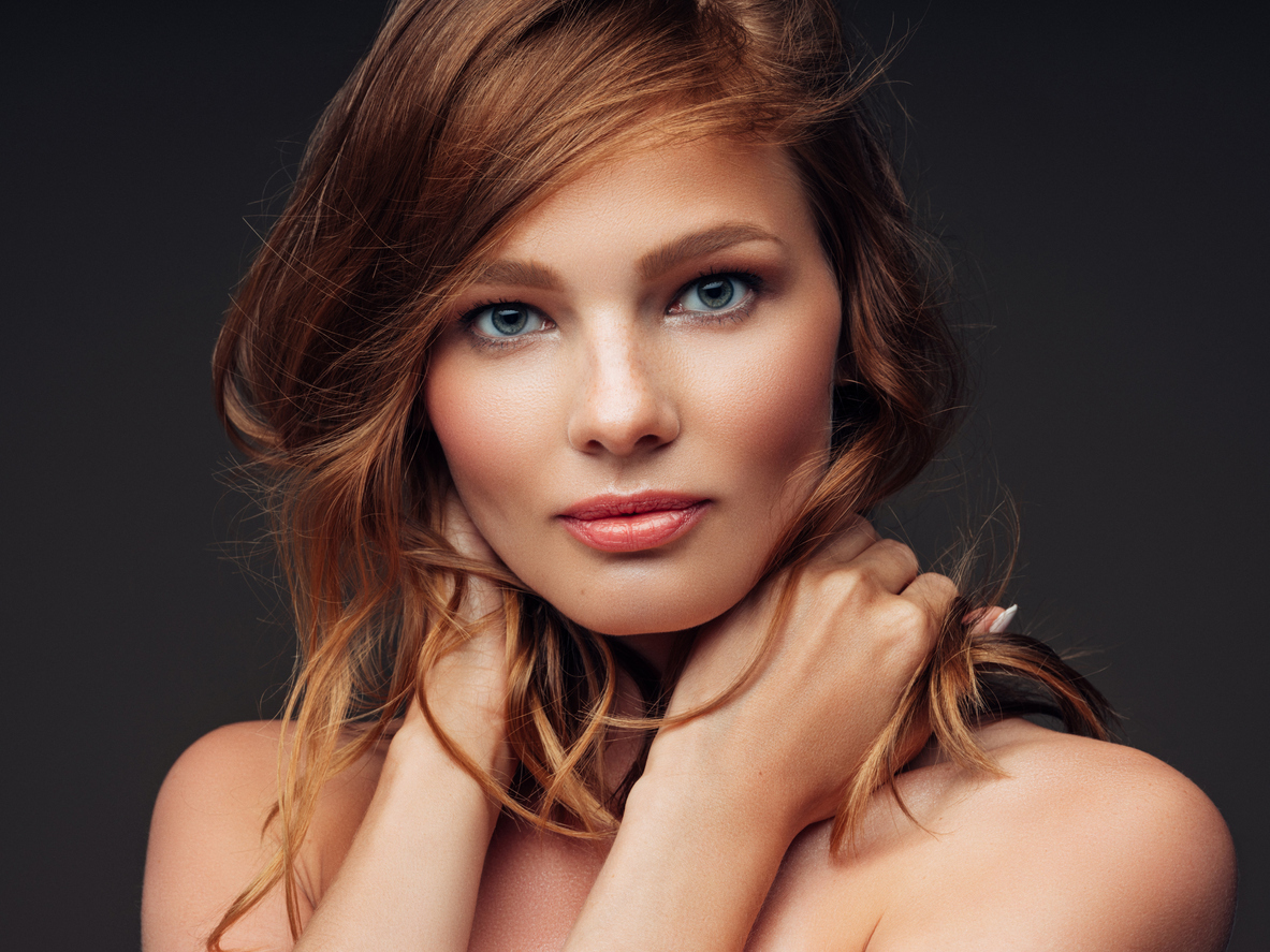 Portrait of a young woman with auburn hair holding her hair at her neck