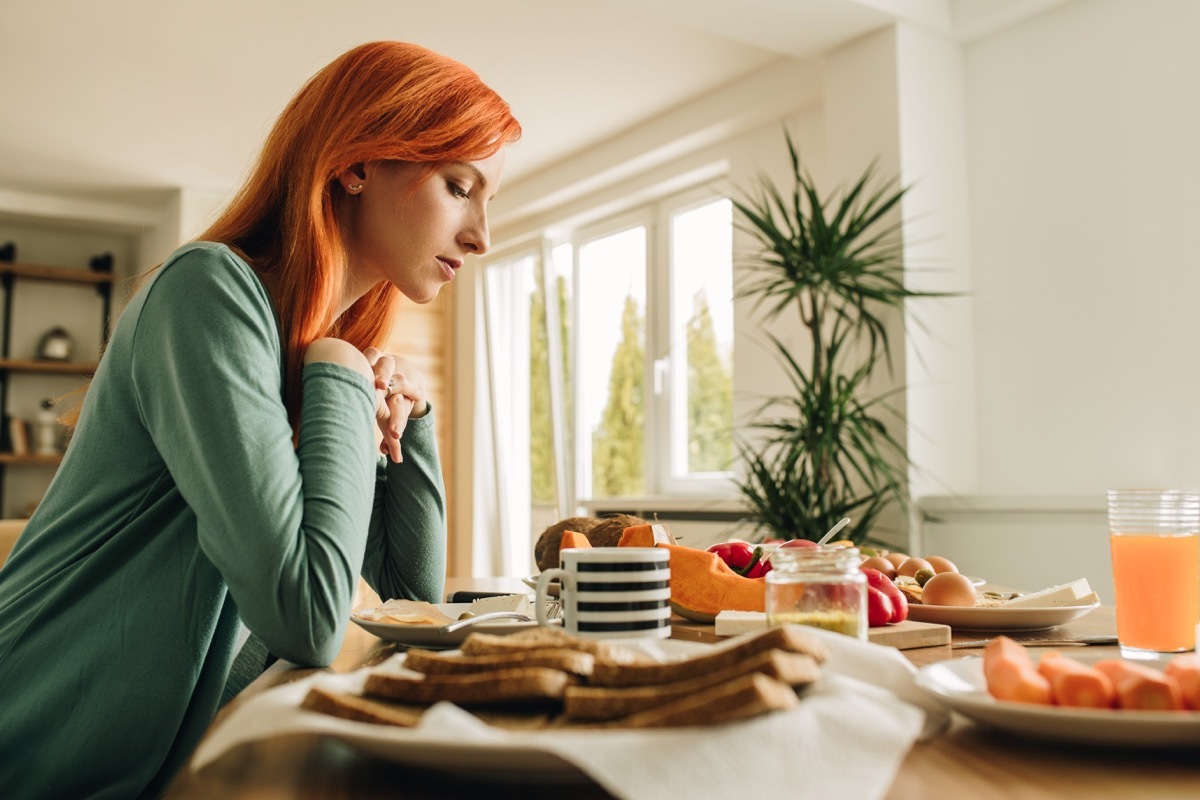 Lonely redhead woman sitting at dining table and thinking of something.